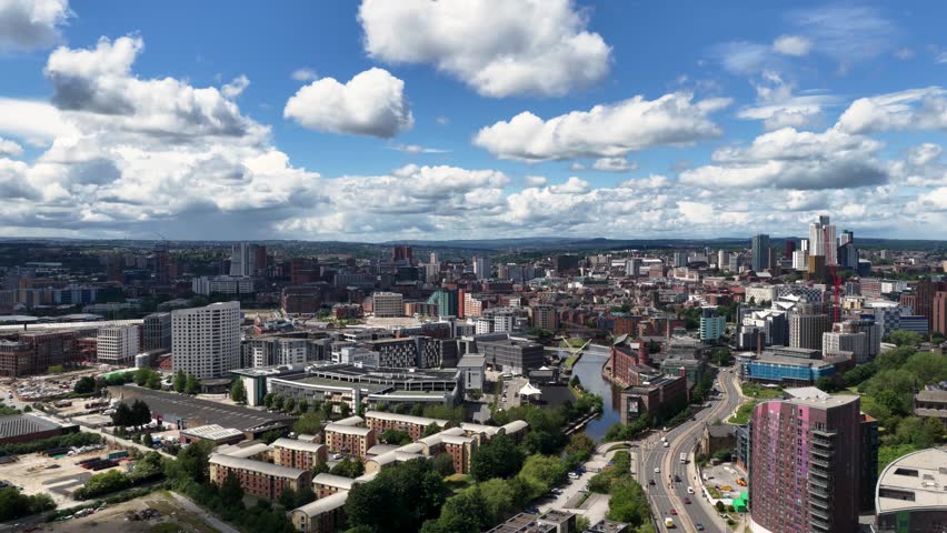 Panoramic aerial view across Leeds city centre featuring the Leeds and Liverpool Canal modern skyline residential developments commercial buildings and urban regeneration under dramatic summer clouds