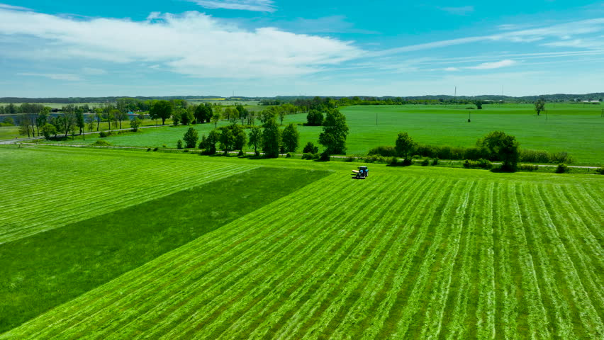 Aerial shot of a tractor harvesting grass in green fields of Lidzbark, Poland. Great for agriculture and sustainability themes.