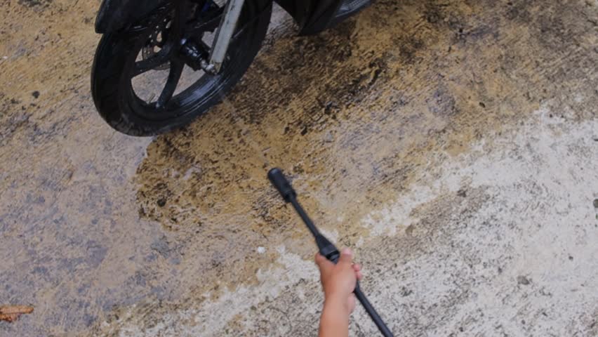 Close-up of motorcycle owner cleaning dirty motorcycle tires with jet washer outdoors