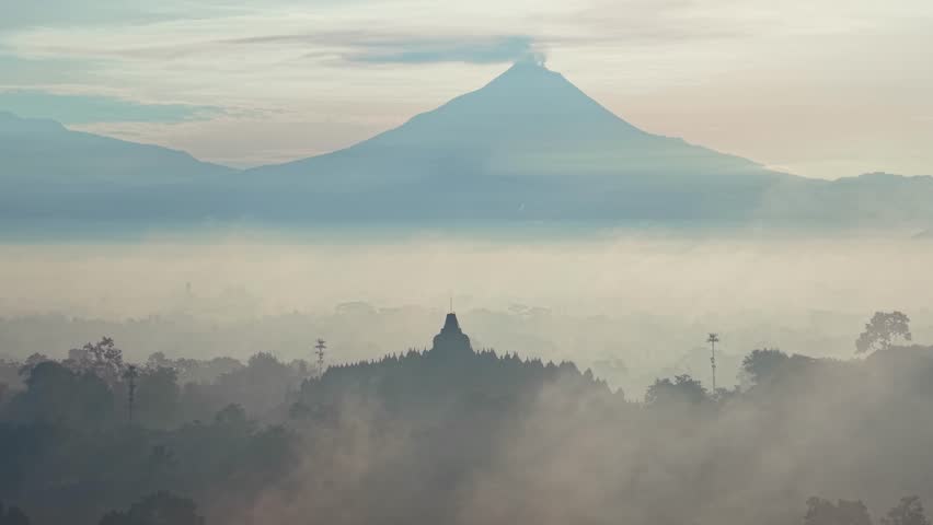 Borobudur Temple surrounded by mist at sunrise with a mountain in the distance, highlighting Indonesia’s cultural landmark and scenic atmosphere.