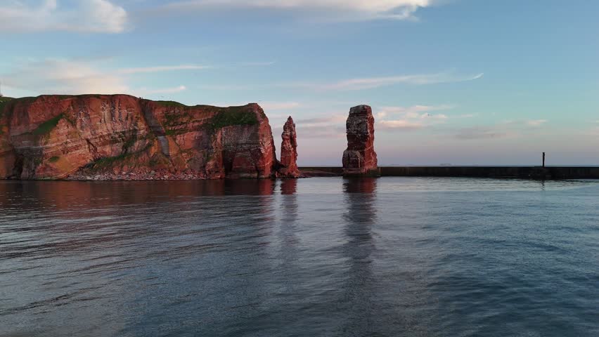 Drone flies toward the small offshore rock and Lange Anna in warm evening light.