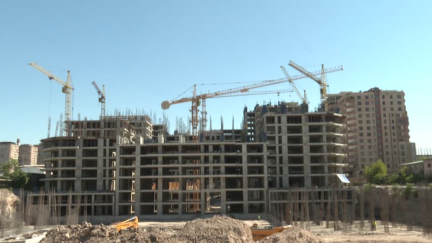 Multiple tower cranes dominate a huge urban construction site. Workers actively build new high-rise residential and commercial buildings, signifying modern infrastructure development and city growth.