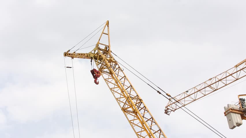 Large yellow cranes operate above stacked rusty scaffolding on a busy construction site. This heavy machinery signifies major urban development and building industry progress.