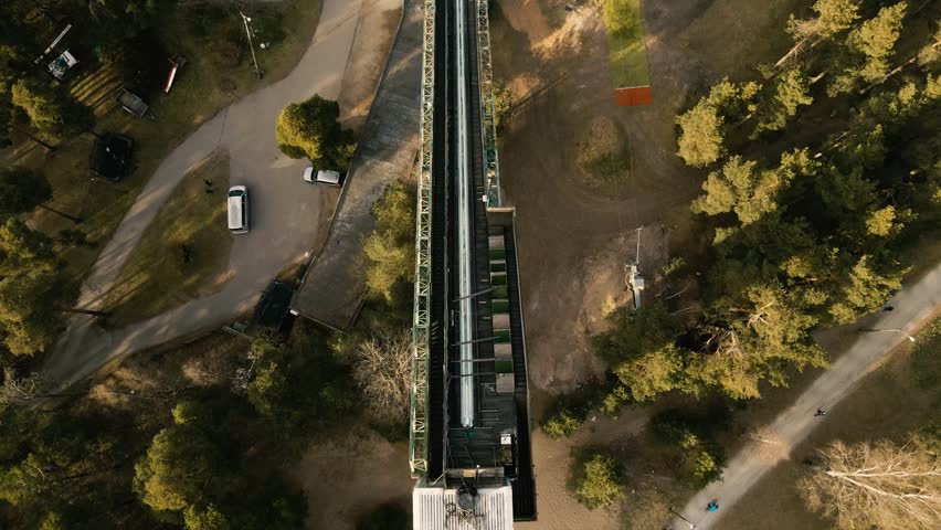 Top down aerial view slowly moving backwards over an old ski jump ramp surrounded by a pine forest. Sports complex seen from above