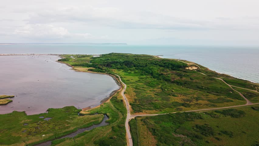 Drone footage looking across Hengistbury Head nature reserve with Christchurch Harbour wetlands woodland heathland coastal paths turquoise sea and distant Isle of Wight coastline.