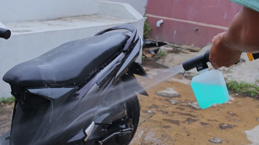 Close up of powerful water spray nozzle cleaning dirt off motorcycle frame outdoors