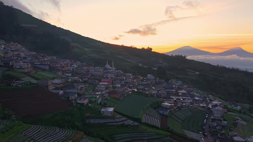 Aerial sunrise view of a mountain hillside village with dramatic sky and rural landscape. Serene countryside scenery with morning light and clouds. Nepal Van Java, Indonesia.