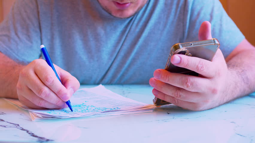 Cinematic close up shot of using a cellphone screen to cross-reference data on paperwork with a felt pen.Visualizes distance learning, accounting, verification and business planning.