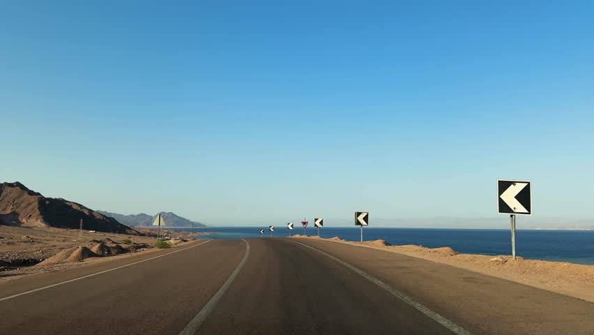 Pov car motion on desert coastal road along the sea with mountains and warning signs