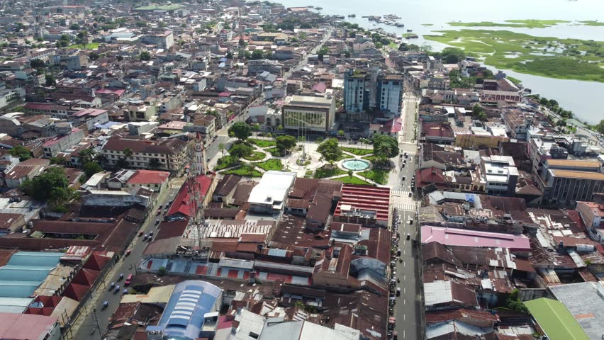 An aerial view showcasing the vibrant and dynamic urban scene of Iquitos, Peru, with its mix of residential structures, modern skyscrapers, and green lawns in the center.