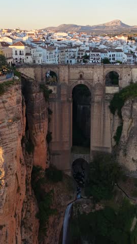 Vertical drone aerial view of Puente Nuevo Bridge spanning El Tajo Gorge in Ronda, Spain with the waterfall cascading beneath the historic landmark