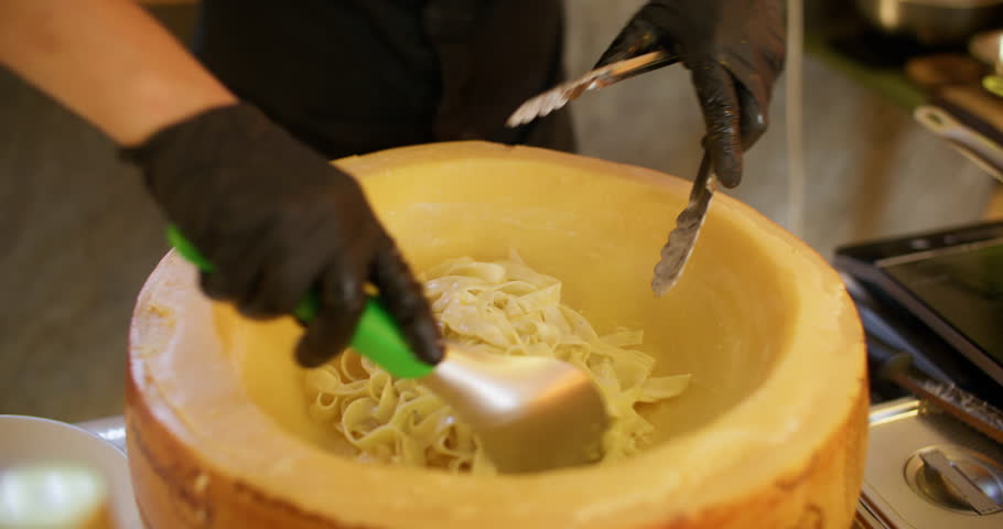 Spaghetti cooking. Italian cuisine. Chef mixing hot fettuccine in parmesan cheese wheel with melted creamy sauce making tasty gourmet dish.