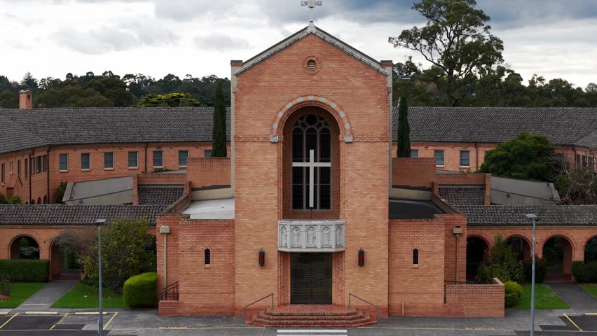 Aerial shot approaching a modern brick church with a large cross on its facade