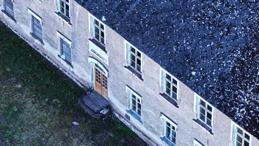 Aerial view of an old abandoned mansion with a tiled roof and boarded-up windows