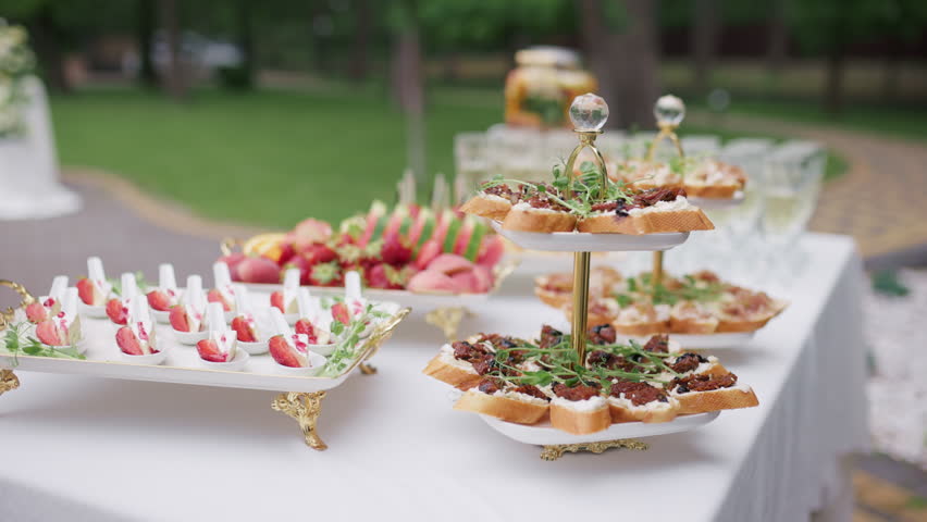 Elegant catering buffet table with gourmet appetizers and drinks outdoors, steadicam shot