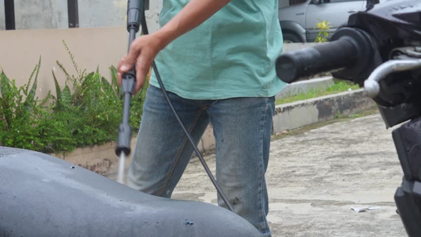 Close-up of hands using pressure washer to clean motorcycle with water spray at outdoor