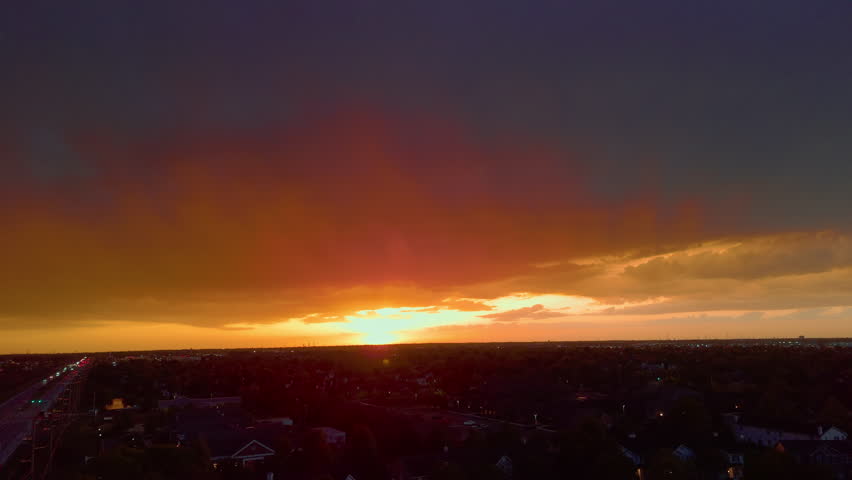 Orange sunset with dramatic clouds glowing above distant landscape during golden hour evening sky at dusk