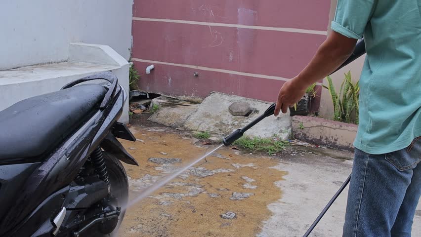 Man cleaning motorbike using power washer stream during weekend routine outdoors