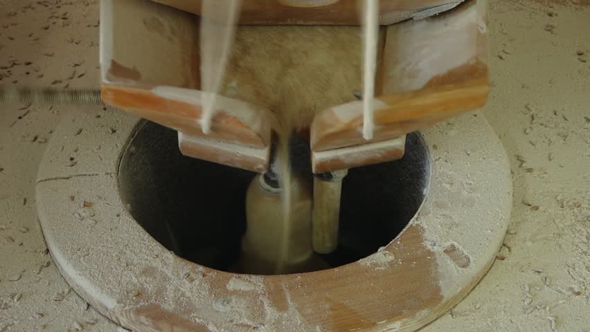 Close-up of a traditional flour mill in action, with grain being ground into flour through a wooden mechanism and fine dust around the milling area.
