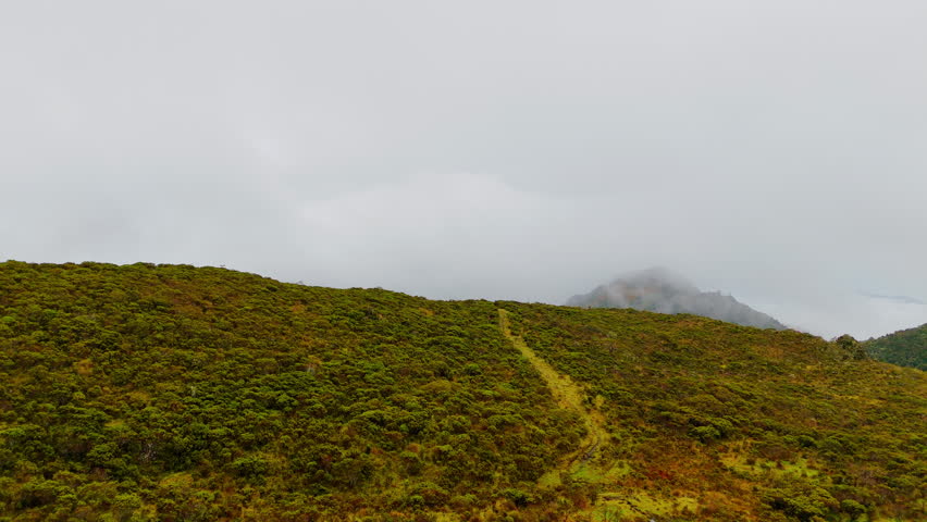 Forward reveal drone flight over foggy Andean mountain slopes near Murillo Colombia. Mountain path visible, volcanic highland terrain, cinematic aerial landscape.