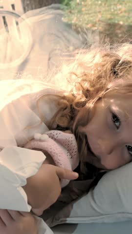 Child is sleeping. cute little girl. beautiful little Princess, in an embrace with a doll, lies on a pillow near the window. sunny day.