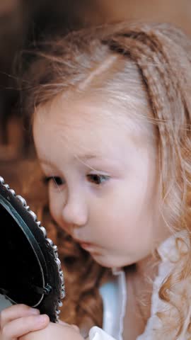 Child admires in mirror. cute little girl. portrait. little Princess. a little pretty girl with blond curly hair admires herself in the mirror