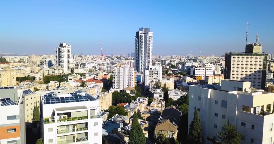Drone shot descending over the urban skyline of Ramat Gan in central Israel. The aerial view reveals a dense metropolitan landscape of residential buildings, office towers, and modern architecture str