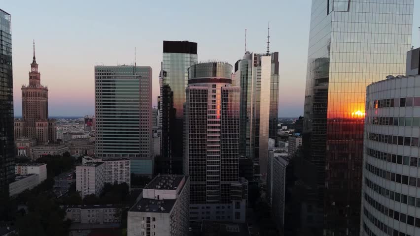 Warsaw - A panoramic view of the city during a summer sunset, the golden hour, with the sun reflecting off the glass facades of office towers. We slowly move away from the city’s business district, seeing more and more of the downtown area and Wola