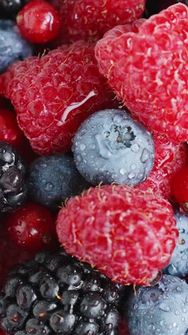 Mixed berries macro close-up water drops vertical raspberry blueberry blackberry redcurrant fresh wet organic food photography texture vibrant red blue slow motion healthy nutrition summer
