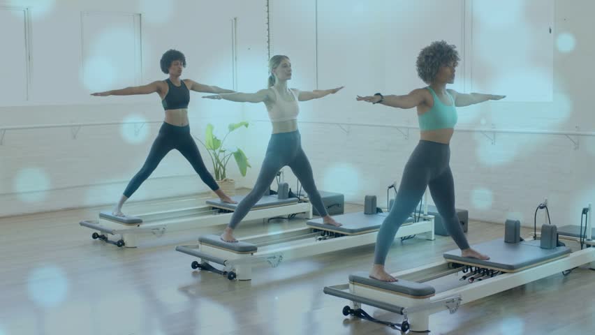On class cue three women doing Pilates shifting carriage for balance, bokeh accentuating motion. Reformer, trio, women, studio, fitness, alignment, stability