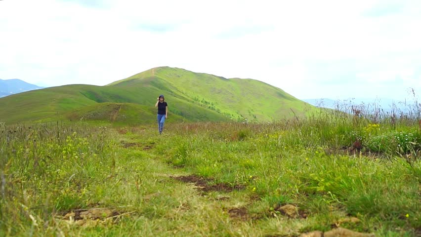 Woman descends a gentle slope from Konjoder summit, looking around as she moves. Shows the reflective journey down, post-summit mindfulness, and the unhurried return through Zlatibor highland terrain.