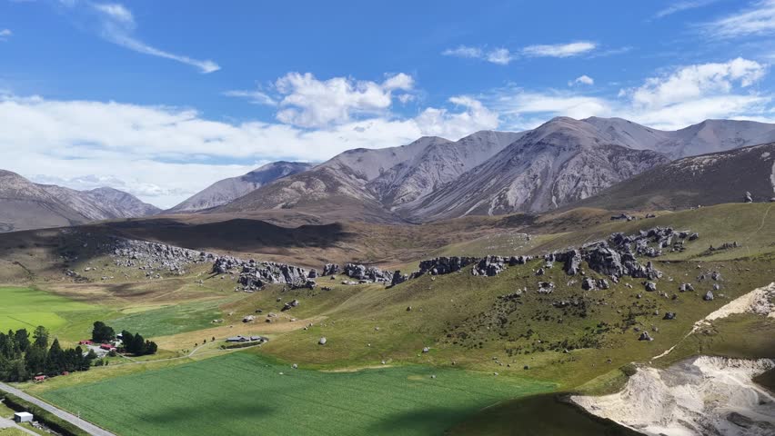 Sweeping aerial view of New Zealand’s South Island featuring alpine foothills, green farmland, and rugged mountain ridges under a bright blue sky.