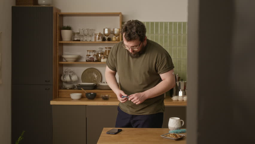 Caucasian middle aged man with diabetes injecting insulin into abdomen with pen injector in kitchen and checking smartphone. Clip ideal for healthcare campaigns and diabetes awareness videos