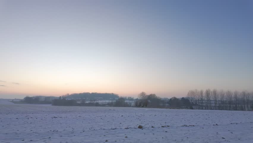 Peaceful Winter Landscape at Twilight - Snow Covered Rural Field with Bare Trees and Farm Buildings in Distance