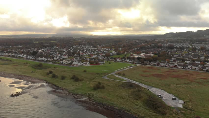 Aerial drone over Doonfoot, Ayr — beach, estuary and housing estate in autumn dusk light, Scotland.