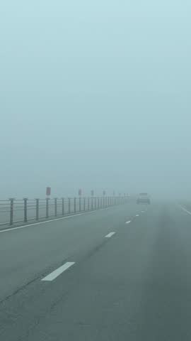 Foggy highway scene with a lone car disappearing into thick mist, creating atmospheric background video