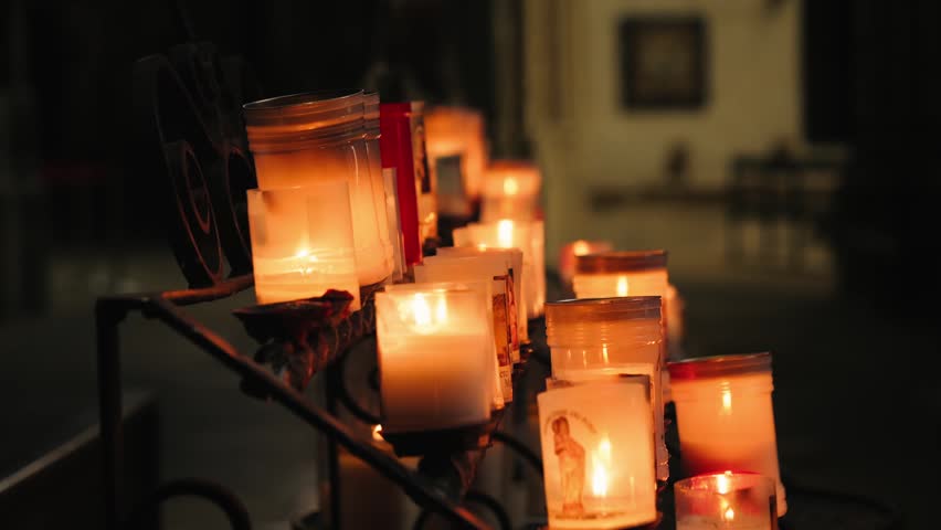 Lit candles glowing in the dark inside a cathedral. A peaceful religious scene with a concept of faith and prayer. High quality 4k footage