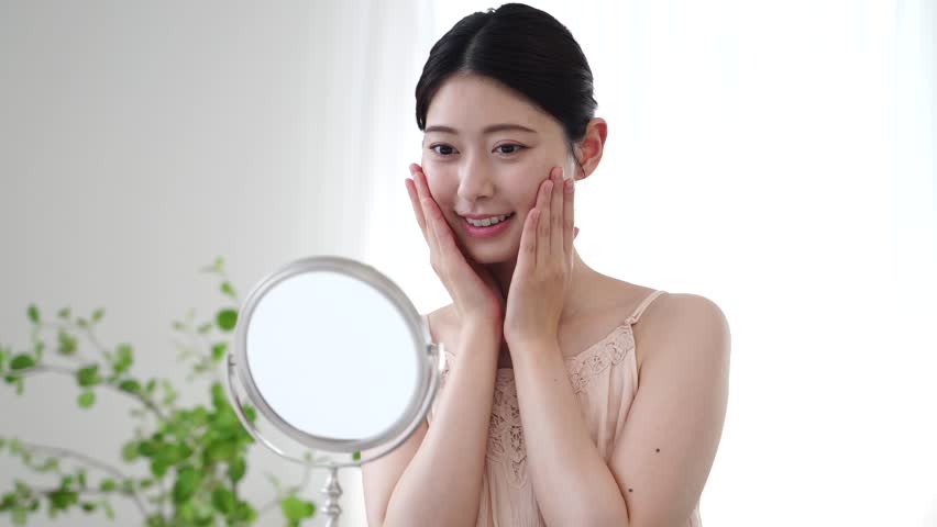 Asian woman doing facial skincare in front of a mirror at home