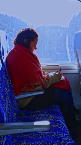 Focused young woman sitting by the window on a moving train, writing notes in her journal while a snowy winter landscape passes by, creating a thoughtful and inspiring travel atmosphere