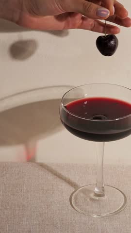 Hand holding cherry over wine glass