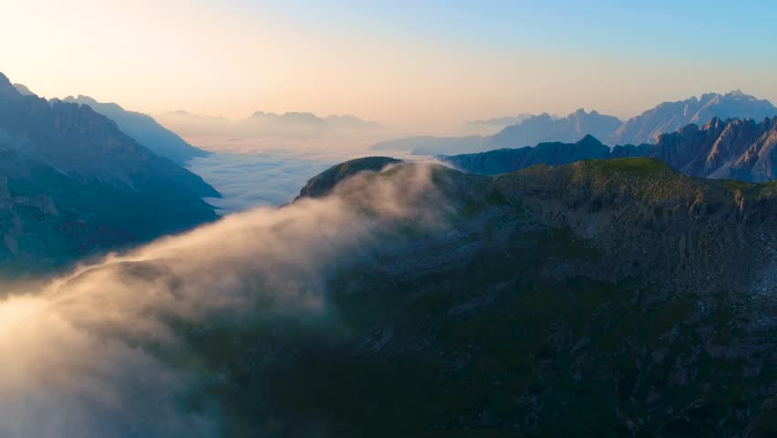 Aerial view of mountain range above clouds during sunrise.