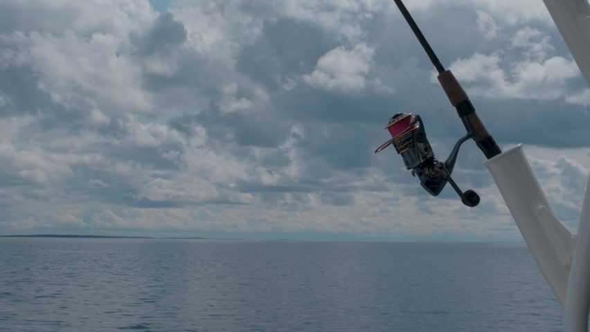 A fishing rod in the foreground as a boat cruises across a vast northern lake surrounded by forest