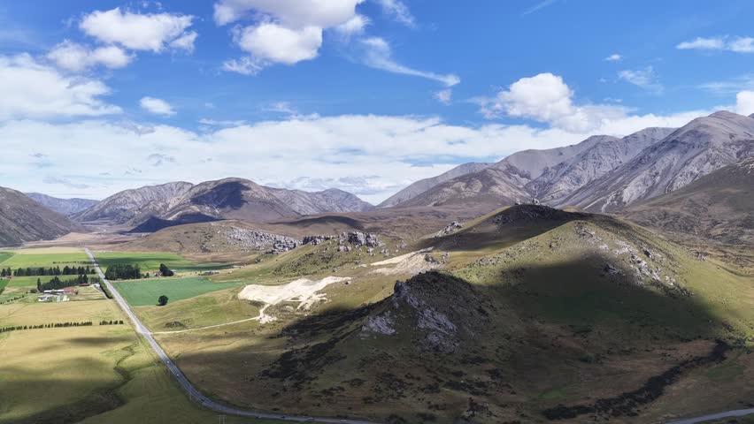 Aerial view of rolling grassy hills, farmland, and mountain backdrop under blue sky