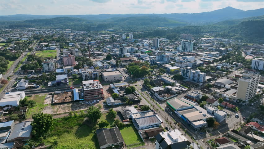Aerial forward push over the central urban corridor of Estancia Velha, Brazil, showing downtown buildings and tree-lined streets.