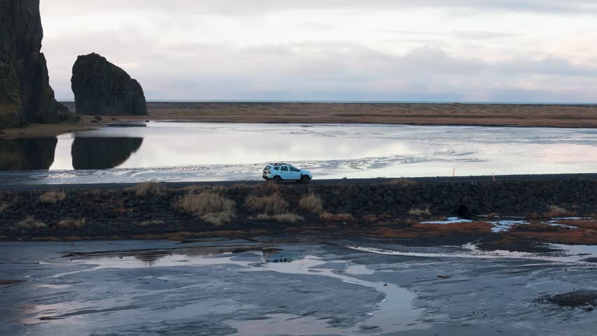 Car driving along scenic black sand beach with unique rock scene Iceland