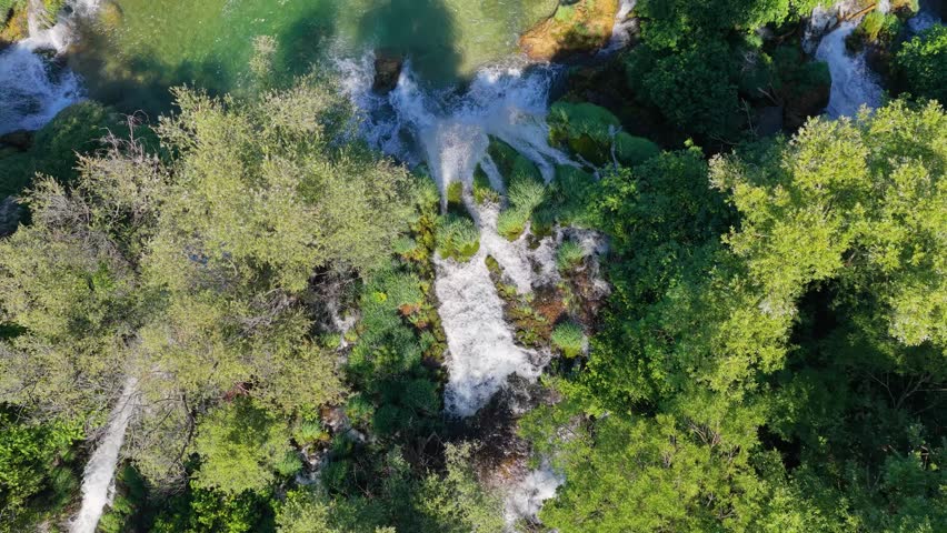 Top-down aerial footage of waterfalls flowing into clear turquoise water surrounded by dense vegetation