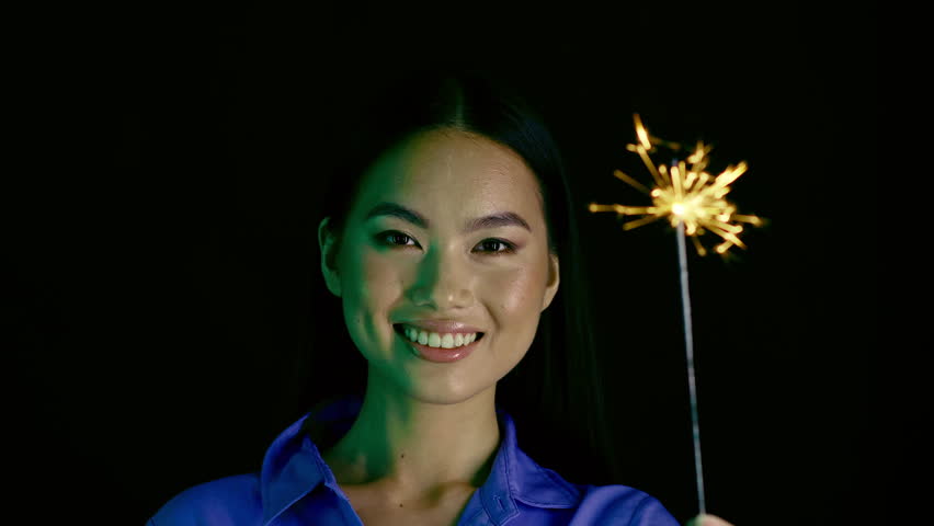 Smiling Asian Woman Holding Sparkler, Celebrating With Joy, Studio Background