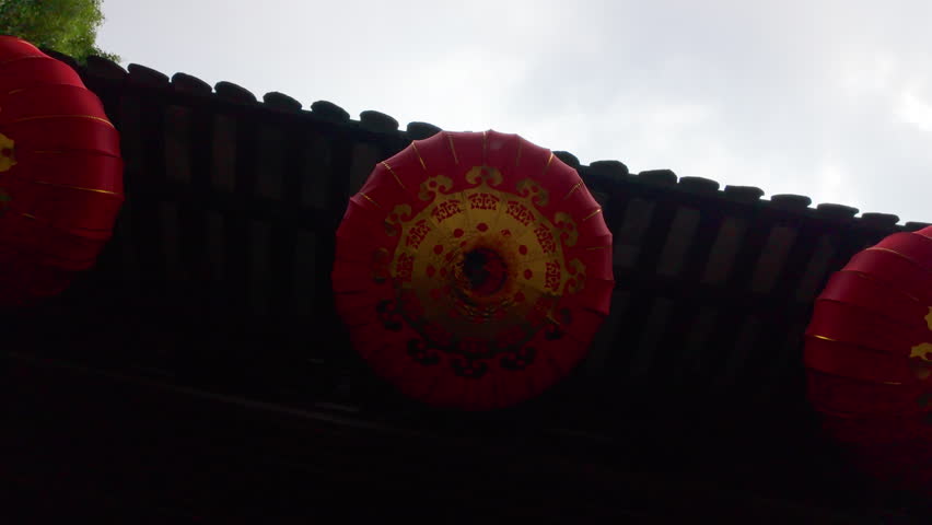 Red decorative lanterns hang under a tiled roof with overcast sky in the background