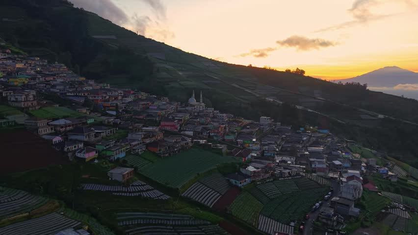 Aerial view of village at sunrise, hillside homes and terraced farms under golden morning light. Nepal Van Java, Indonesia.