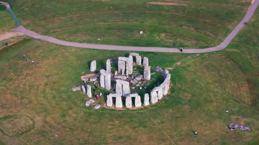 Aerial footage of Stonehenge in Wiltshire, England, showing the ancient stone circle, surrounding grassland, visitor paths and open landscape. Historic landmark footage useful for travel, heritage,